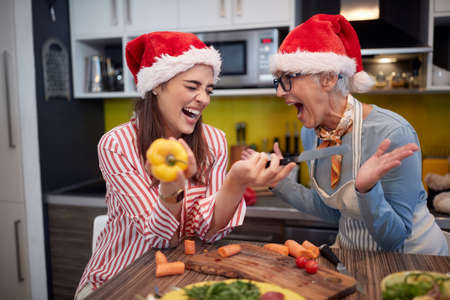 Mother and daughter joking while preparing a Xmas meal in a festive atmosphere in the kitchen. Christmas, family, togetherの写真素材