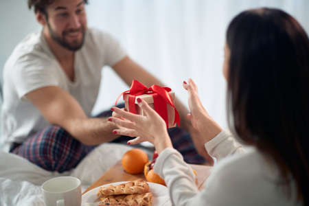 A young guy giving a Xmas present to his girlfriend in the bed on a beautiful holiday morning. Christmas, relationship, love, togetherの写真素材