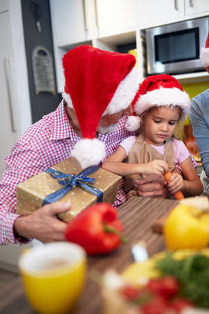 Grandpa in the kitchen in festive atmosphere having a Xmas present for granddaughter. Christmas,...