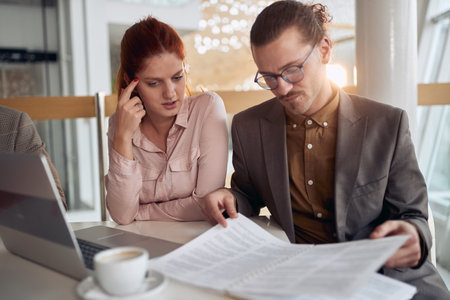 Young colleagues at a break reading documents in a pleasant atmosphere at company canteen. People, job, company, business concept.の写真素材