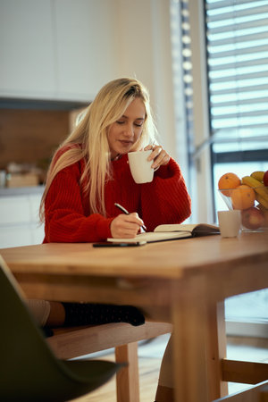 A young girl studying and drinking coffee on a beautiful morning at the kitchen. Routine, student,...