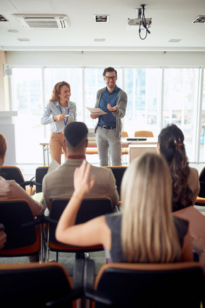 young caucasian manager lecturing at business seminar. blonde female raising hand for question