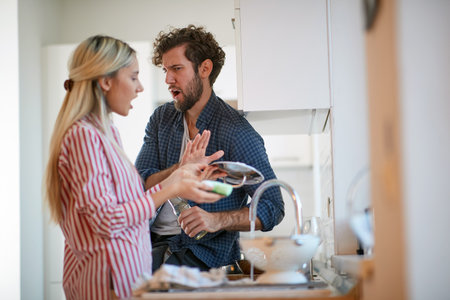 A young couple arguing about housework in a tense atmosphere at the kitchen. Kitchen, housework, home, relationshipの写真素材