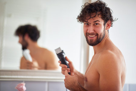 Happy topless man shaving with shaver in the bathroomの写真素材