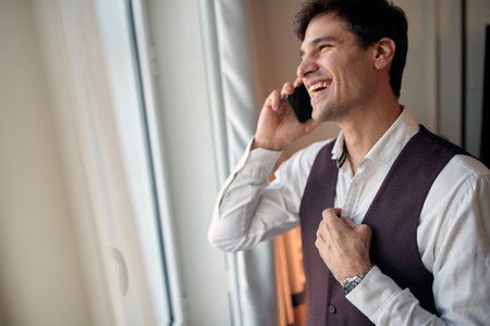 A young businessman at the hotel room preparing for a job and talking over the smartphone on a beautiful morning. Hotel, business, peopleの写真素材
