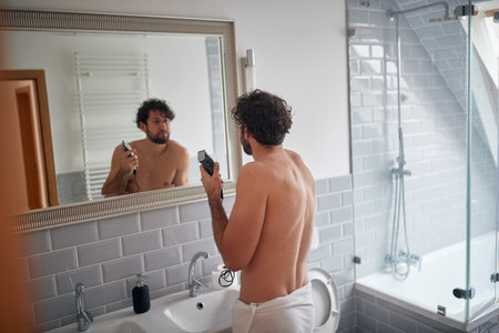 Caucasian topless man shaving with shaver in the bathroomの写真素材