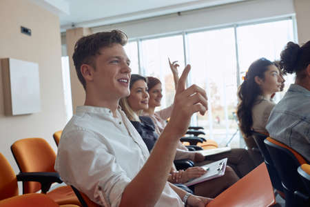 young  caucasian guy at business seminar raising hand, smiling
