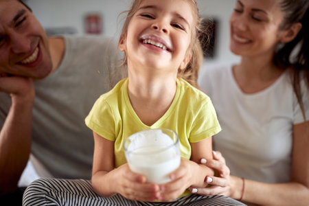 A little girl with her parents in a family atmosphere at home posing for a photo with a glass of yogurt. Family, breakfast, together, homeの写真素材