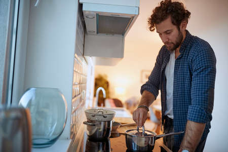 Young man preparing a meal on a stove in a relaxed atmosphere in the kitchen. Kitchen, housework, quarantin, homeの写真素材