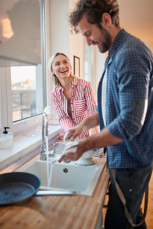 A young couple having a good time doing housework in a cheerful atmosphere in the kitchen together. Kitchen, housework, home, relationshipの写真素材
