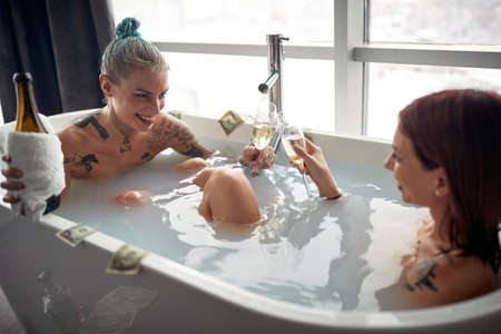 A young sexy tattooed lesbian couple enjoying champagne while having a bath in a relaxed atmosphere...