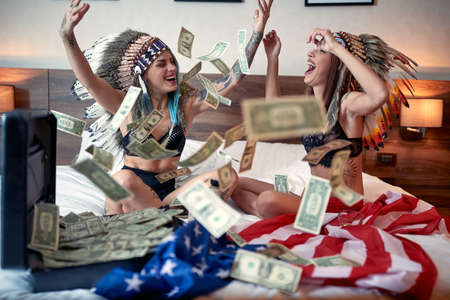 A young tattooed lesbian couple in the lingerie in a relaxed atmosphere in the bedroom throwing the money and yelling while celebrating the successes in the promised land. Love, lgbt, USA, luxury, relationshipの写真素材