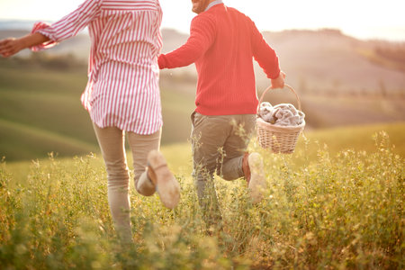 A young couple holding by hands and running over a large meadow on a beautiful sunny day. Love, relationship, together, natureの写真素材