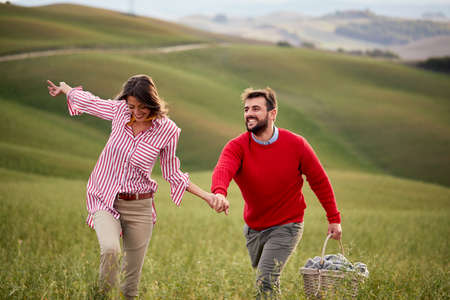 A young couple is enjoying nature while walking a large meadow by holding hands on a beautiful day....