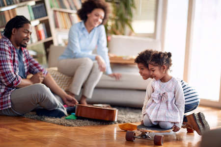 Kids riding skateboard on the floor and enjoying the playtime with their parents in a cheerful atmosphere at home. Family, together, love, playtimeの写真素材