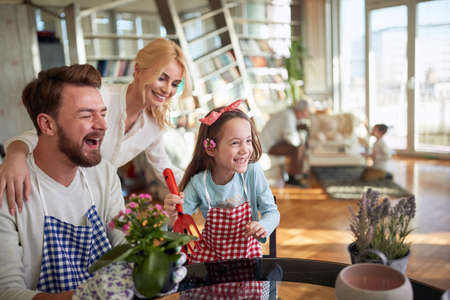 A little daughter has wonderful time with her parents while planting flowers together in a cheerful atmosphere at home. Family, leisure, togetherの写真素材