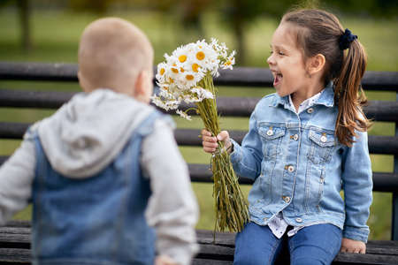 thrilled little caucasian girl looking at bucket of flowers that her preschooler friend gave her.の写真素材