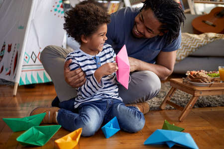 A young father and his cute little son spending a wonderful time together while playing with paper boats in a playful atmosphere at home. Family, home, playtimeの写真素材
