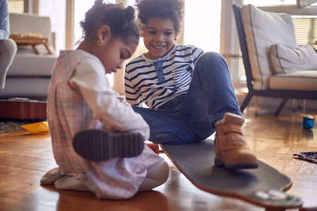 Cute little brother and sister sitting on the floor in a playful atmosphere at home and playing with the skateboard. Family, home, playtimeの写真素材