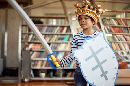 A cheerful little boy posing with a sword and a shield while playing in a relaxed atmosphere at home. Family, home, playtimeの写真素材