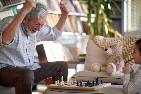 A happy grandpa enjoys playing a chess game with his little grandson in a relaxed atmosphere at home. Family, home, playtimeの写真素材