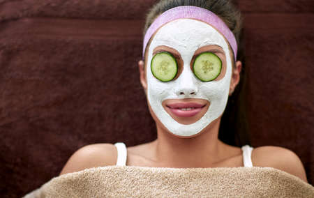 Smiling woman with cosmetic mask and cucumber on eyes, regenerationの写真素材