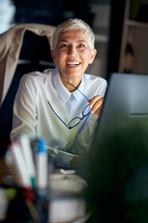 A senior business woman is posing for a photo at the desk in a pleasant atmosphere at the workplace. Business, office, jobの写真素材