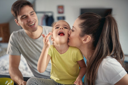A little girl enjoying the love from her parents during a breakfast in a cheerful atmosphere at home. Family, breakfast, together, homeの写真素材