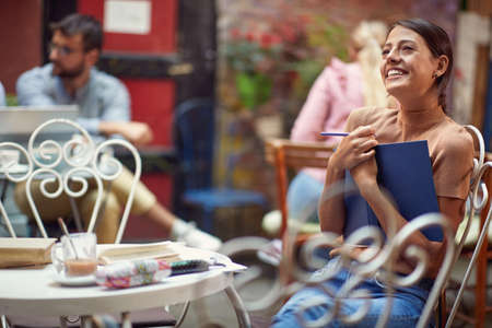 A young female student has an inspiration to write on a beautiful day at bar's garden. Leisure, bar, friendship, outdoorの写真素材