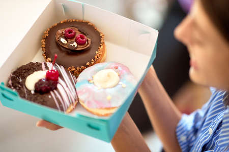 A beautiful girl in a pleasant atmosphere of a pastry shop is holding a box with delicious donuts....