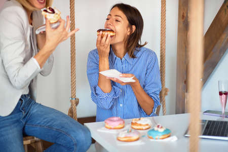 Two female friends enjoy eating delicious donuts in a pleasant atmosphere in a pastry shop. Pastry...