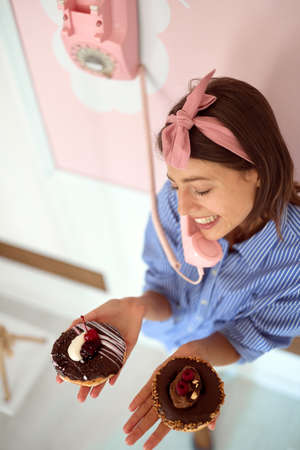 Shot from above of a young beautiful girl holding chocolate donuts in her hand and having an...