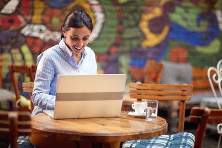 A young female student is working on a laptop while having a coffee on a beautiful day at bar's garden. Leisure, bar, outdoorの写真素材