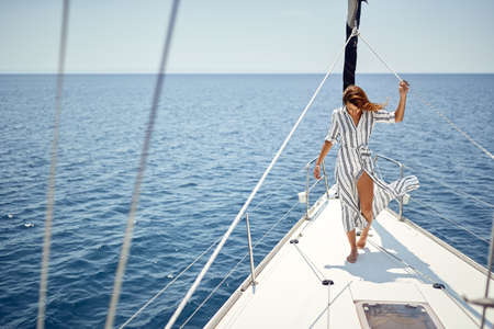 A young handsome barefoot female model standing on the bow of a yacht