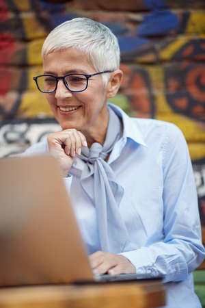 An elderly woman watching a laptop content while spending free time at bar's garden on a beautiful day. Leisure, bar, friendship, outdoorの写真素材