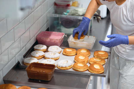 A female worker dips the donuts in a delicious topping in a working atmosphere in a candy workshop. Pastry, dessert, sweet, makingの写真素材