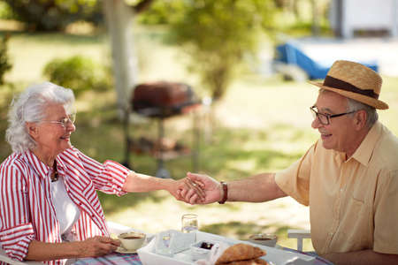 cute elderly couple enjoy outdoor, having breakfast and coffee, holding handsの写真素材