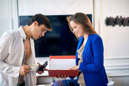 beautiful young business female showing content from a folder to male in a unbutton shirt holding cup of coffee and a cell phone.の写真素材