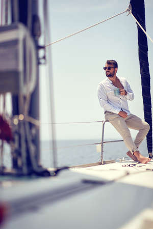A young handsome male model is sitting on a yacht on the seaside and enjoying a photo shooting on a beautiful sunny day. Summer, sea, vacationの写真素材
