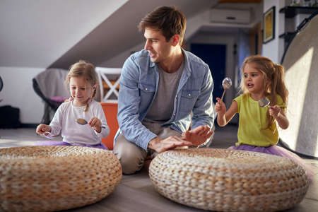 Little daughters with spoons sitting on the floor in a cheerful atmosphere at home and enjoy...
