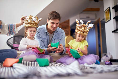 A young family sitting on the floor in a cheerful atmosphere at home and playing with paper boats. Family, together, playtime, homeの写真素材