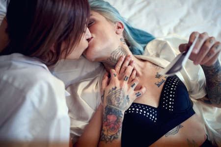 A young happy lesbian couple lying in the bed at home is kissing in satisfaction because they will have a baby. Love, pregnancy, lgbt, relationshipの写真素材