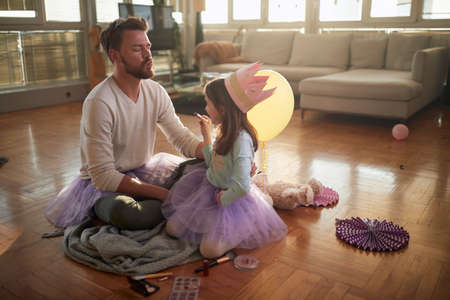 A young father waiting for his little daughter to put some lipstick on his lips while preparing for ballet practice in a relaxed atmosphere at home. Family, together, homeの写真素材