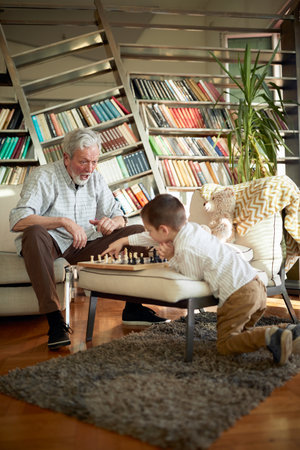 Grandpa is excited when plays the chess with his little grandson in a playful atmosphere at home....
