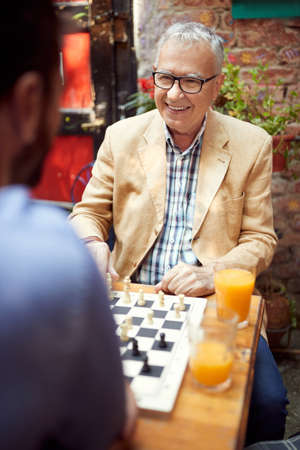 senior good looking caucasian male looking at his younger opponent playing chess , sitting in outdoor cafeの写真素材