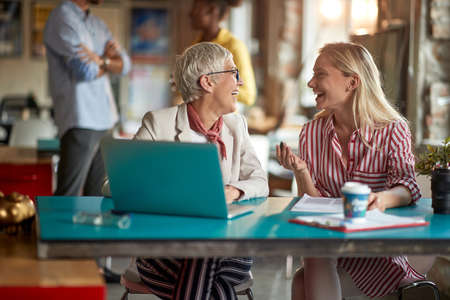 Elderly female boss enjoying a work in a pleasant atmosphere at office with her young female colleague. Employees, office, workの写真素材