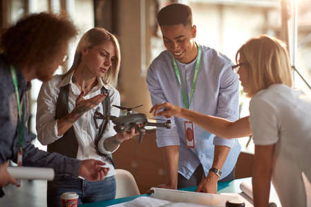 A group of young creative people in a working atmosphere in the office discuss the drone they will...