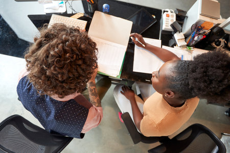 Two young colleagues are sitting in a pleasant atmosphere at office and working on project together. Employees, office, workの写真素材