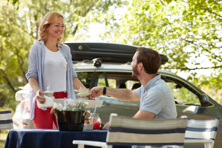 young beardy guy taking cup of coffee from a tray offered by beautiful caucasian blonde female
