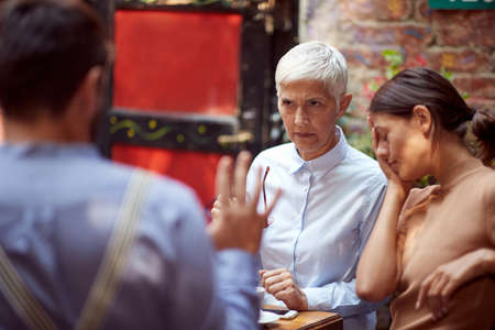 angry mother in law looking reproachfully  her son-in-law who is justifying. her daughter sitting...